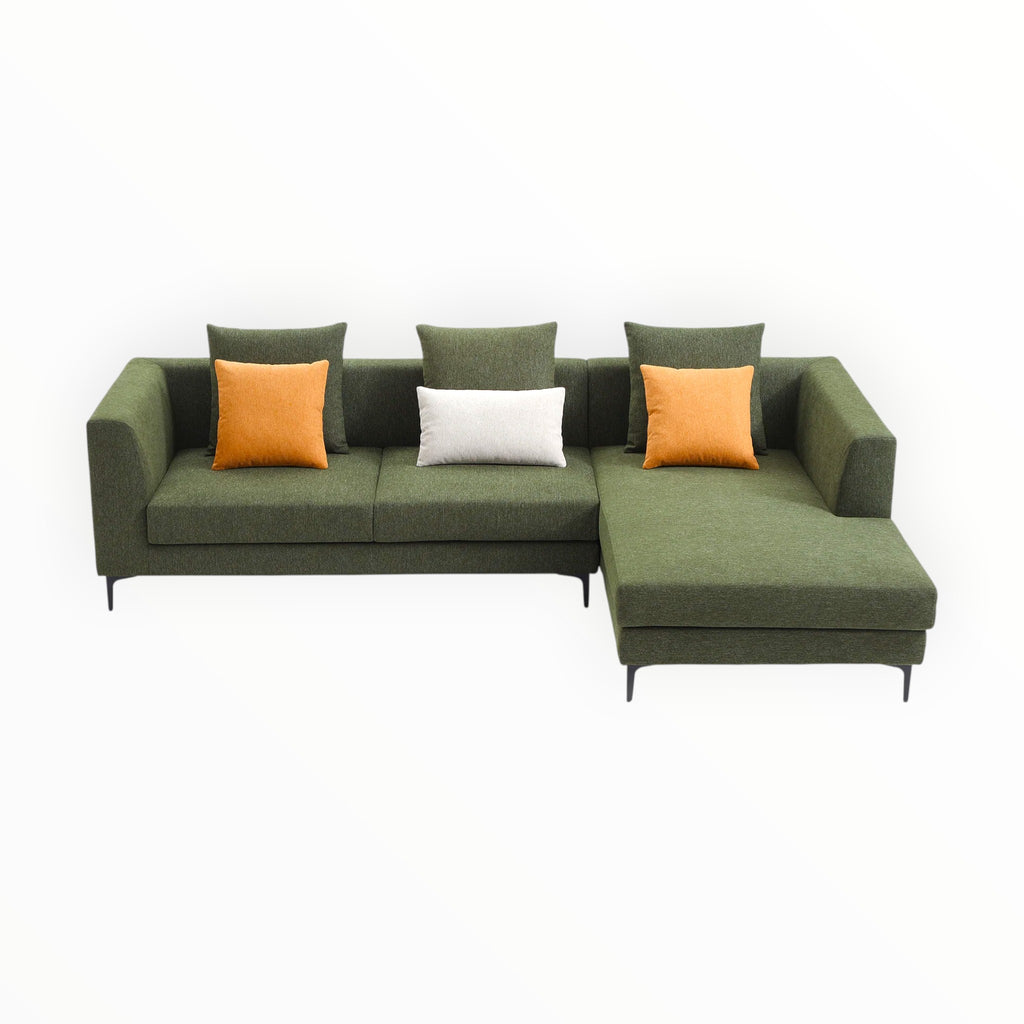 Green sectional sofa with orange and white cushions on a white background