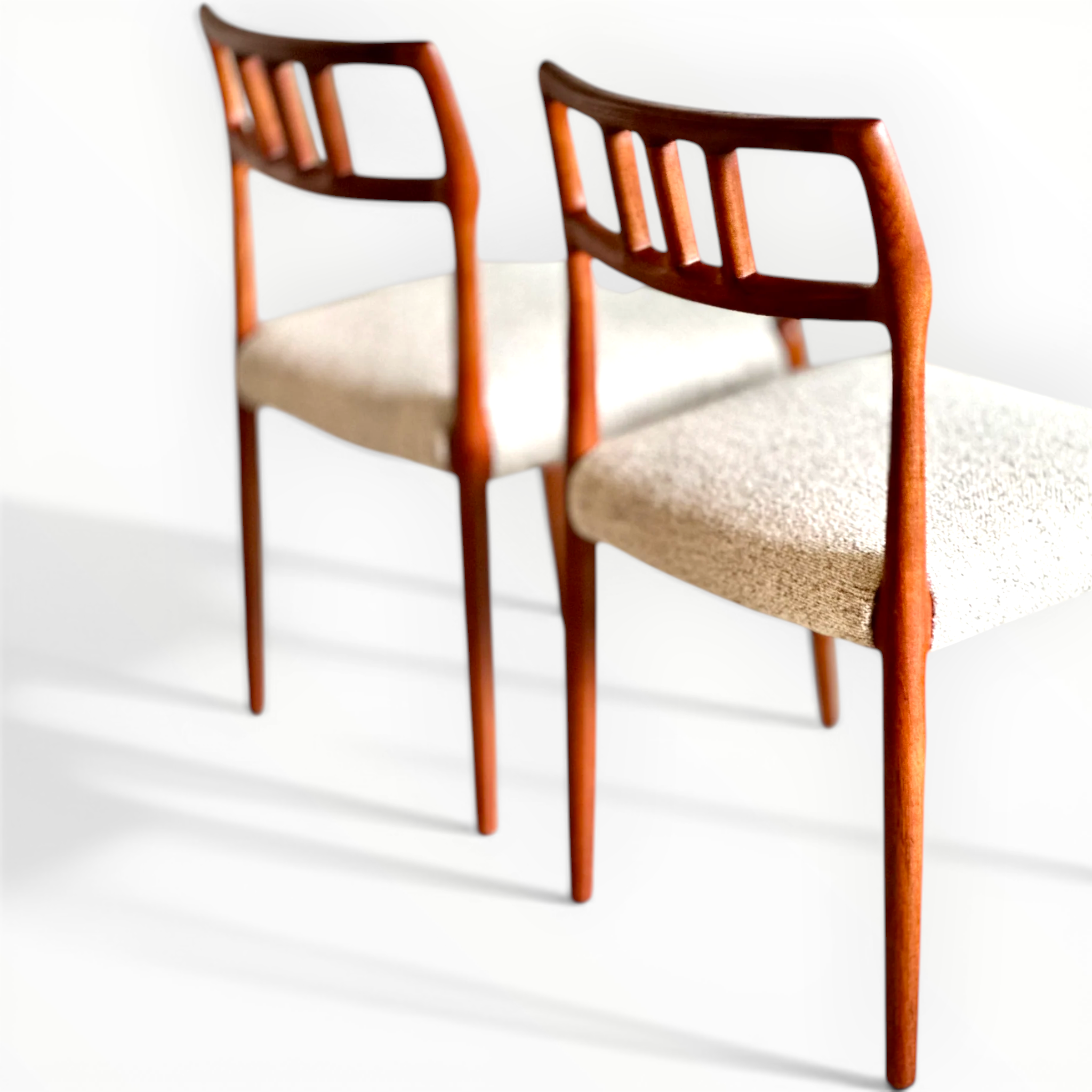Two wooden chairs with beige cushioned seats on a white background