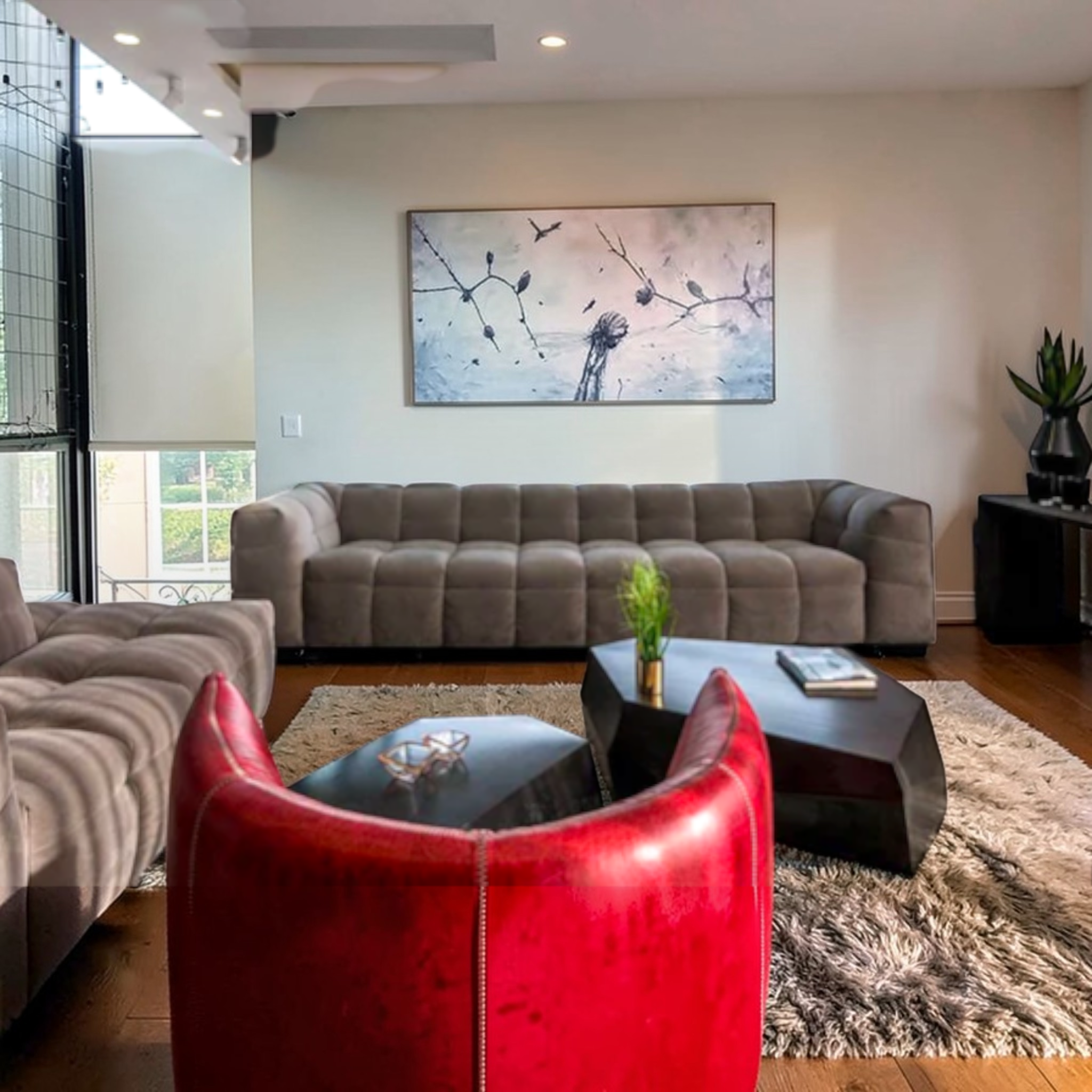 Modern living room with gray sectional sofa, red chair, and abstract wall art.