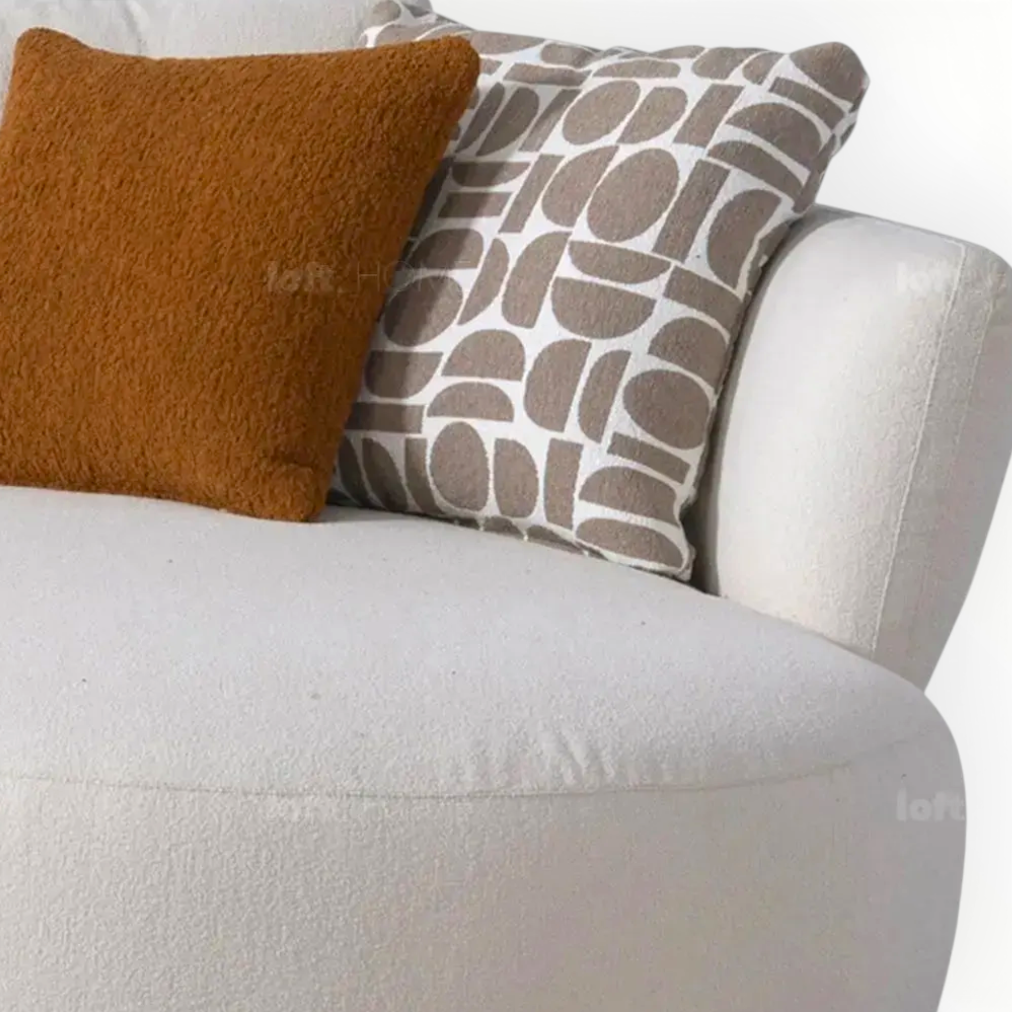 Two pillows, one brown and one with a geometric pattern, on a white sofa.