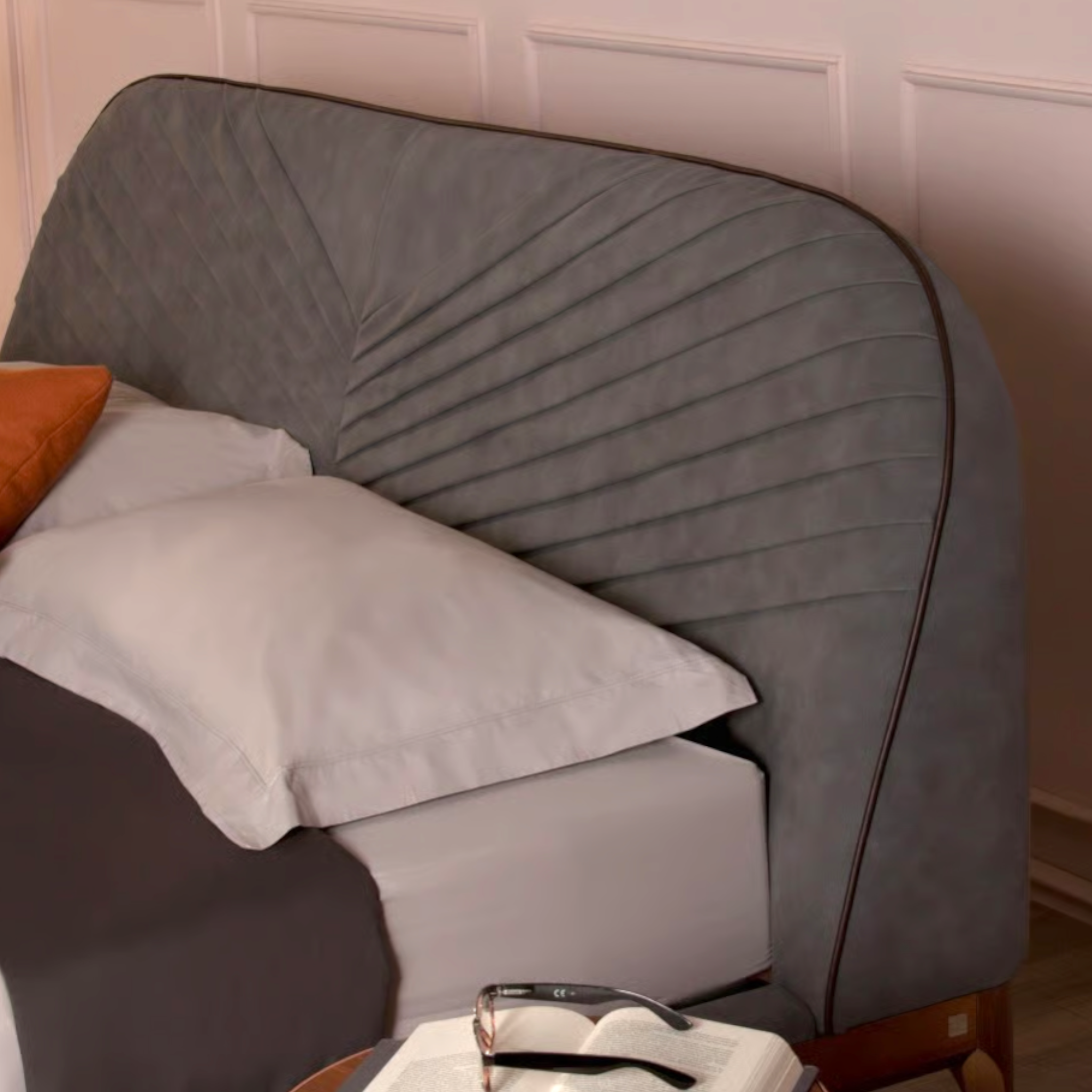 Gray upholstered headboard with pillows against a white paneled wall