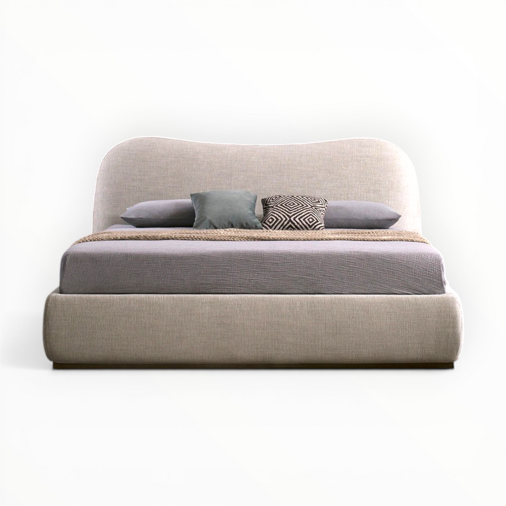Beige upholstered bed with gray bedding and pillows on a white background
