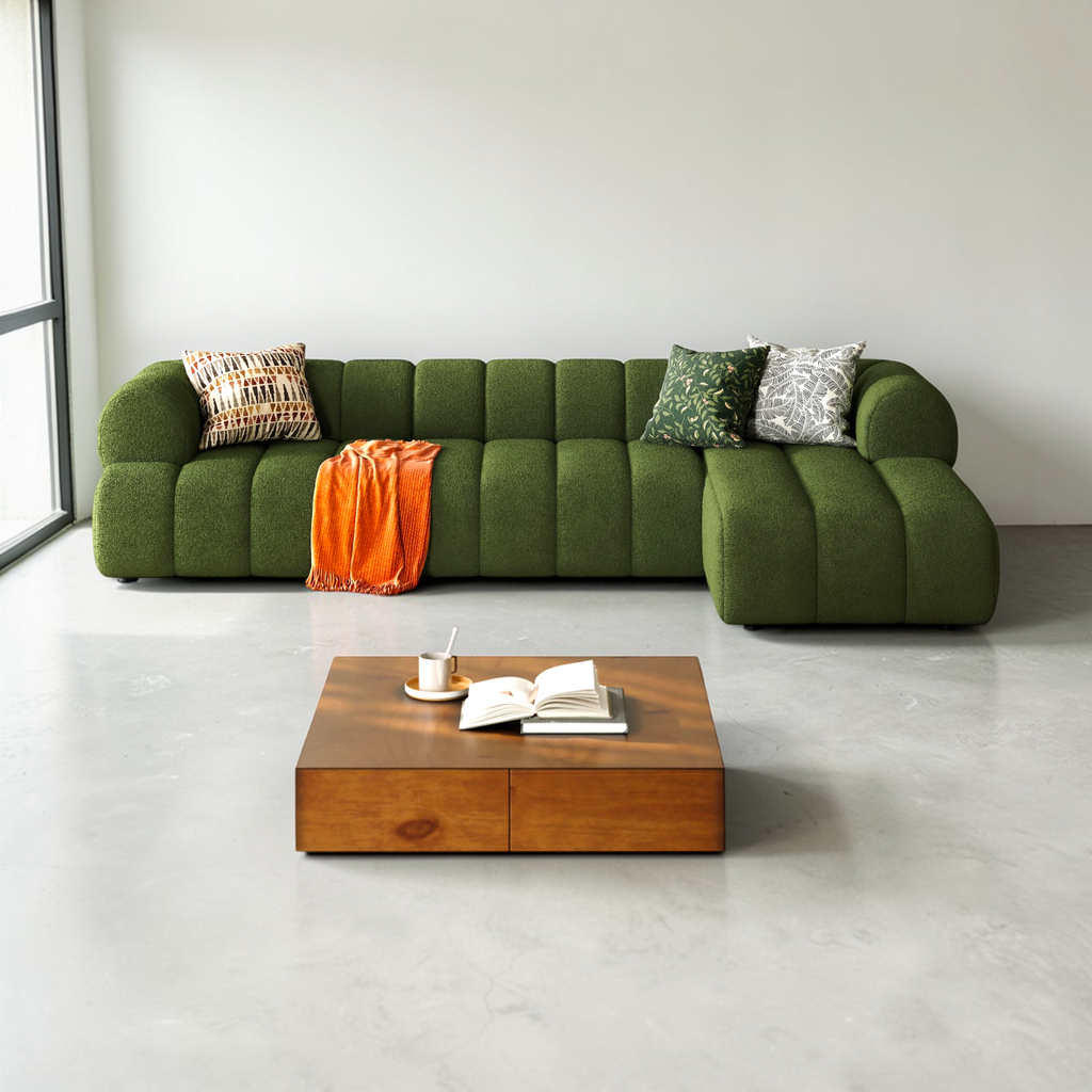 Green sofa with decorative pillows and an orange blanket in a modern living room.