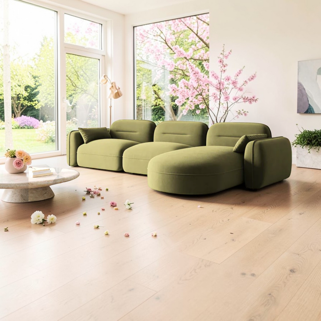 Green sectional sofa in a bright living room with large windows and cherry blossoms outside.