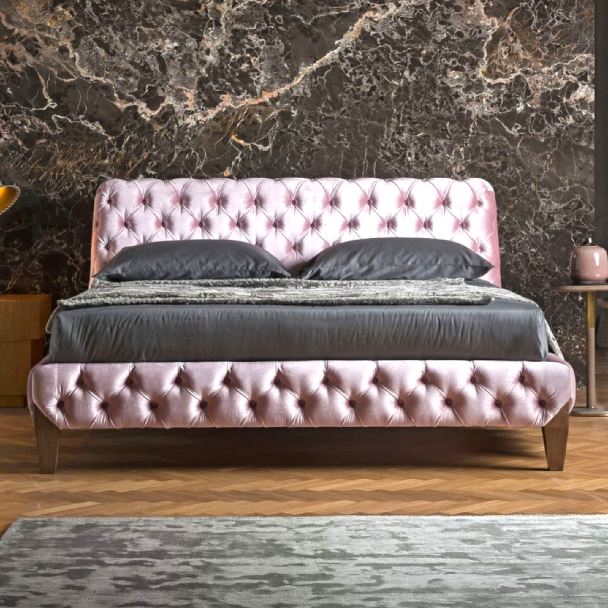 Pink tufted bed with gray bedding against a marble wall.